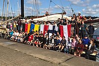 Gruppenfoto, ca. 60 Jugendliche stehen mit den Flaggen von Österreich, Finnland, Polen, Ukraine und Deutschland an Bord eines Segelschiffes.