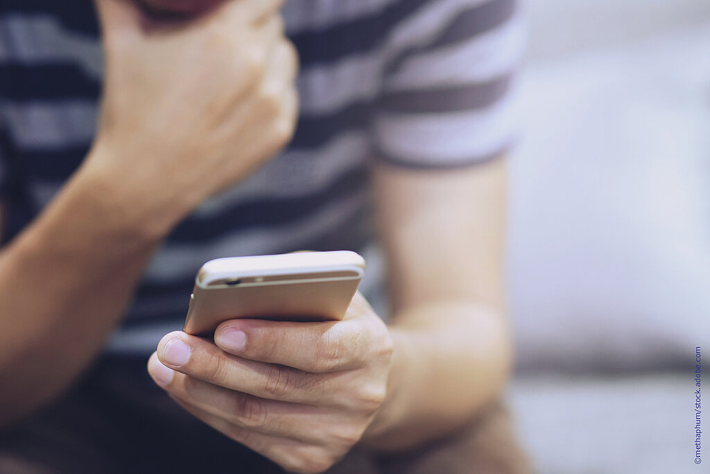 Ein junger Mensch schaut in sein Smartphone.