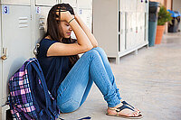 Mädchen sitzt vor einem Schrank im Schulflur